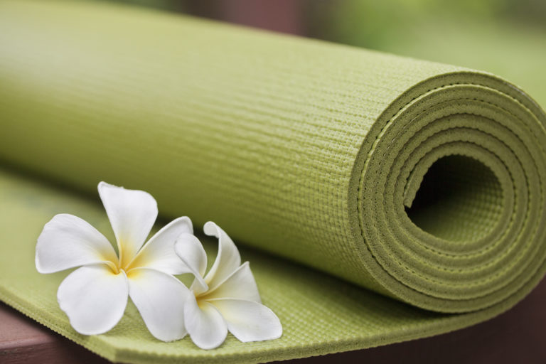 Ausgerollte grüne Yogamatte mit zwei Blüten